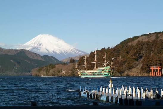 A red torii gate standing in Lake Ashi with Mount Fuji visible in the background in Hakone