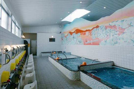 High wood-beamed ceilings and a painted mural of Mount Fuji inside a traditional neighborhood public sento bathhouse in Tokyo